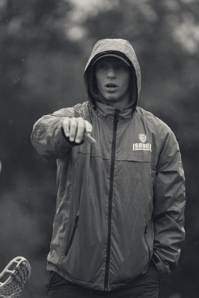 Ashtin Reich, wearing an Israel Lacrosse jacket, pointing while coaching in the rain.